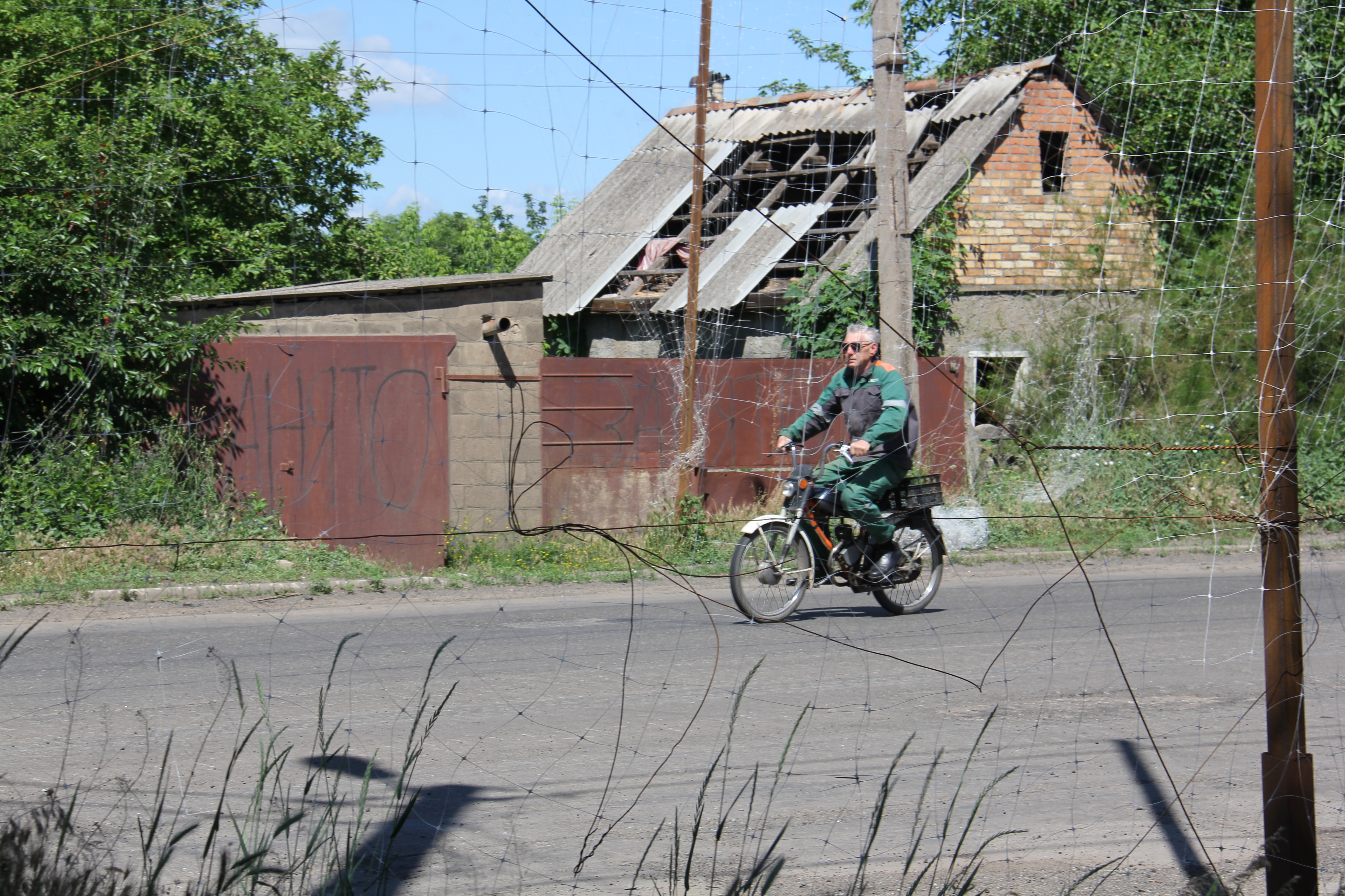 Місцевий житель прифронтового населеного пункту їде на велосипеді по дорозі, вкритій протидроновою сіткою