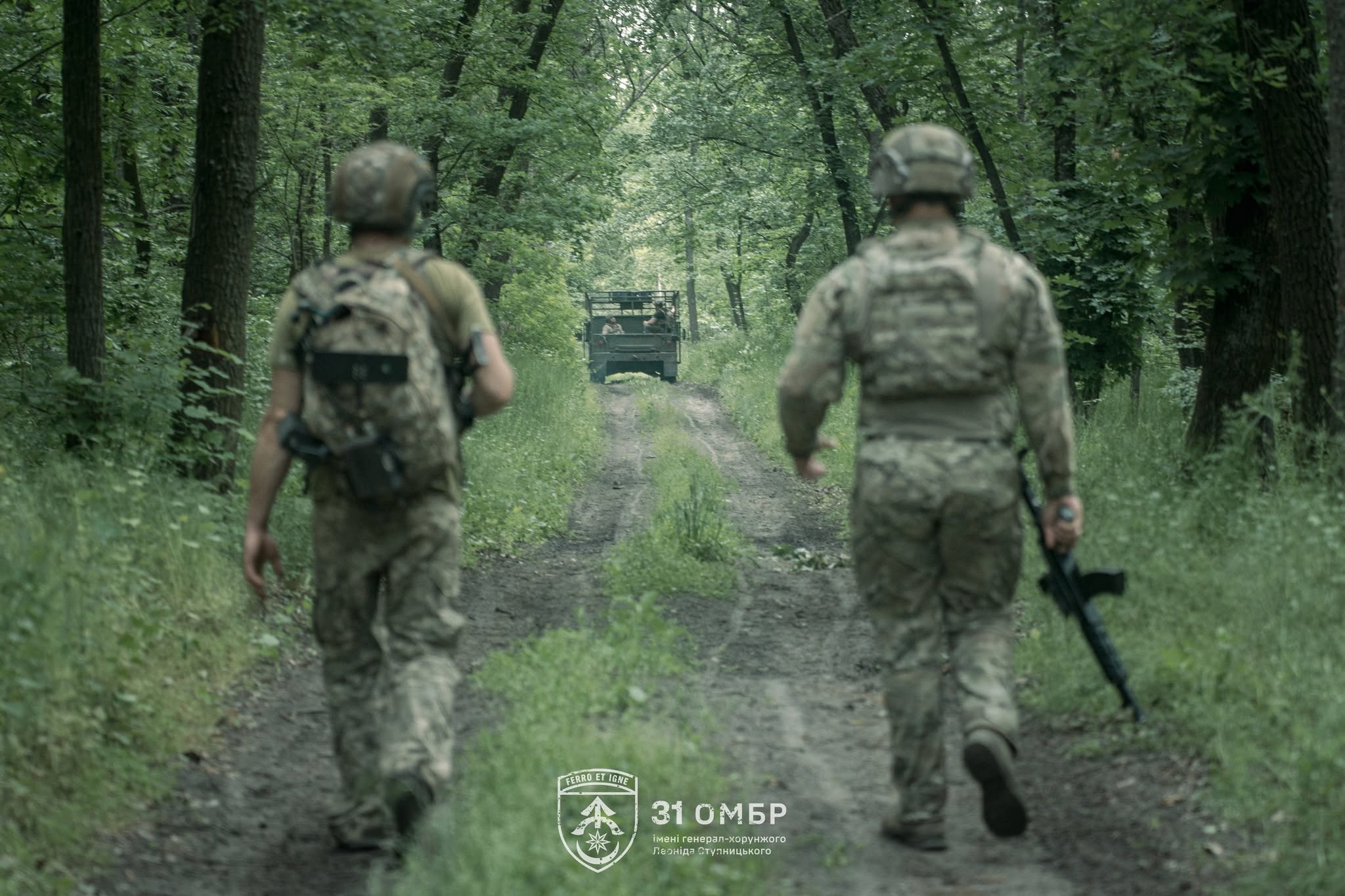 У затемненому приміщенні стоїть двоколісний електричний транспортний засіб військового призначення. Крупний план переднього колеса, фари та керма акцентує увагу на його конструкції та прохідності.