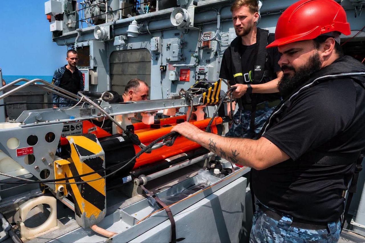 Моряки готують до застосування помаранчевий підводний апарат, закріплений на спусковій конструкції. Вони перевіряють троси, механізми та оснащення перед спуском пристрою у воду.