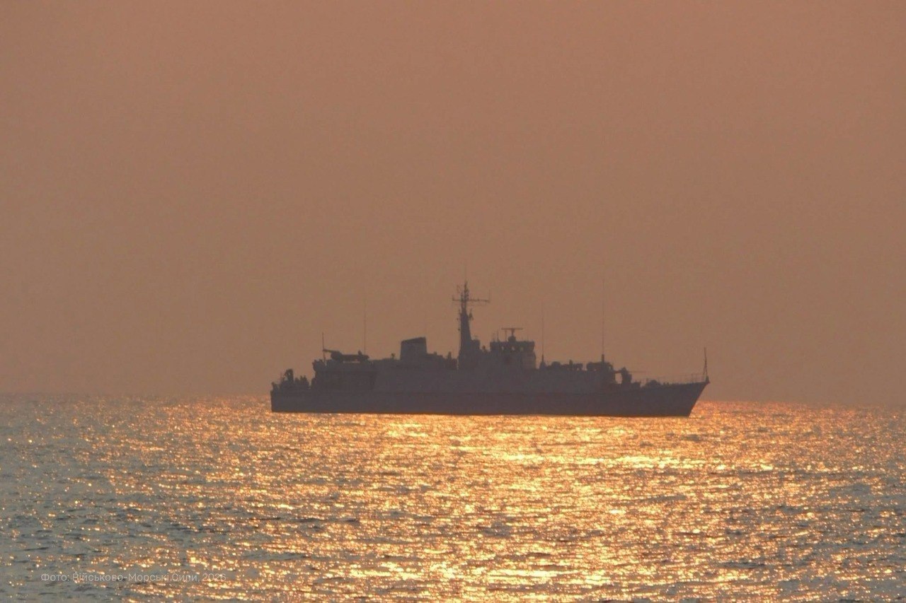 Військовий корабель проходить морем на тлі теплого вечірнього неба. Його силует вирізняється над золотистою поверхнею води, освітленою низьким сонцем.