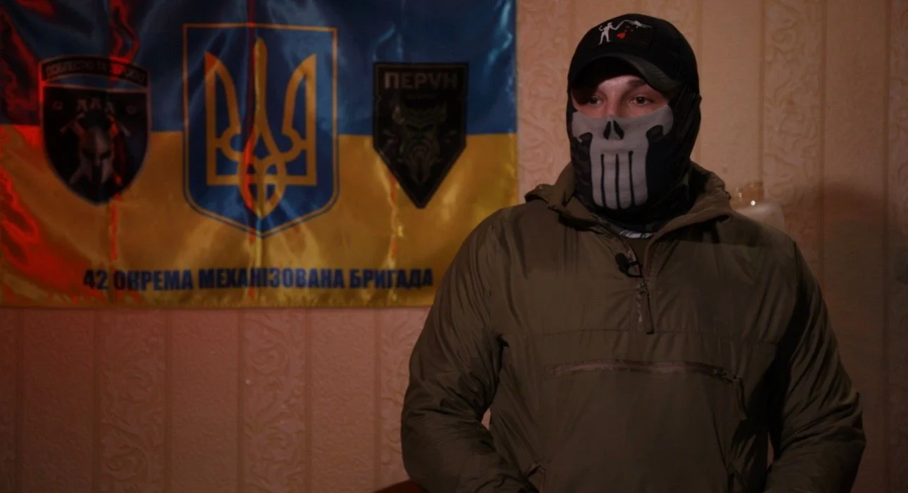 Військовий в балаклаві на фоні прапора